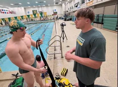 Coach with swimmer standing by an indoor pool before a meet