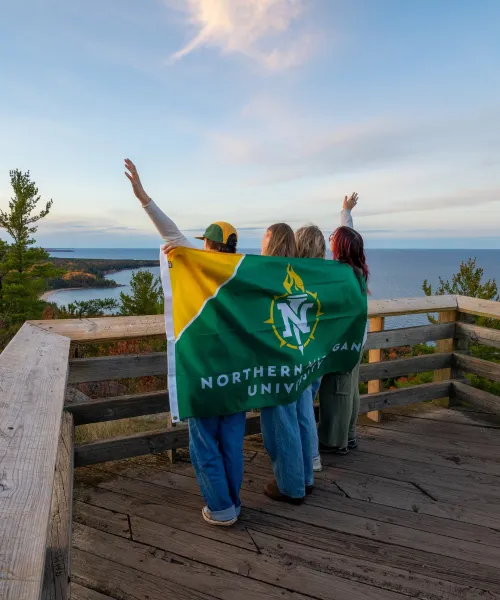 Students at the top of a mountain holding an NMU flag facing away from the camera