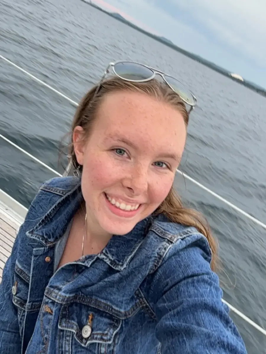 Selfie of a girl in a jean jacket, taken on a boat with the lake as a background.