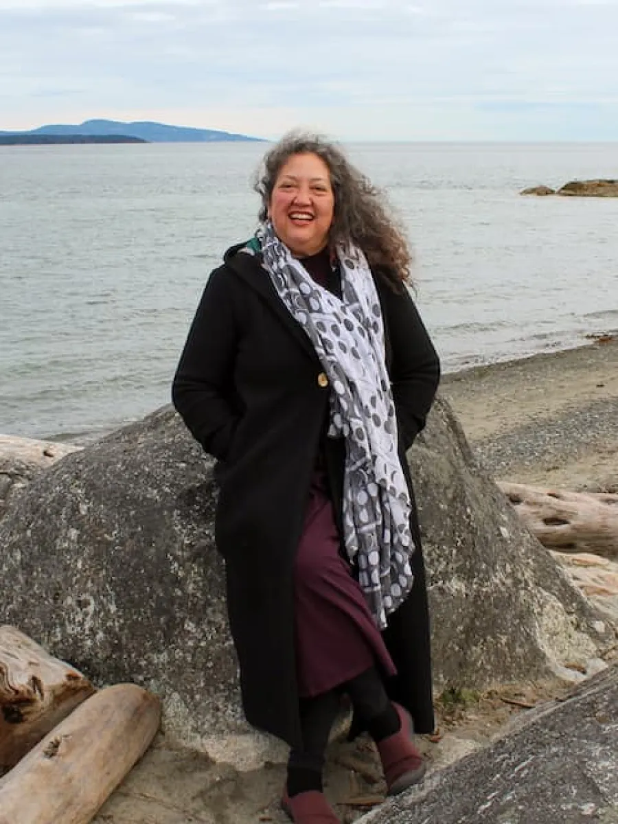 Lisa Hall standing by a body of water leaning on a rock. 
