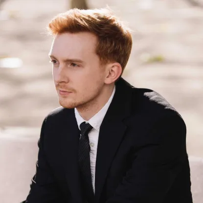 Christopher Goodpasture - concert pianist (publicity photo).  Young man with red hair wearing black suit and long black tie.  Sitting and looking off into the distance.