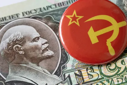 A Soviet hammer-and-sickle pin resting on currency featuring Vladimir Lenin