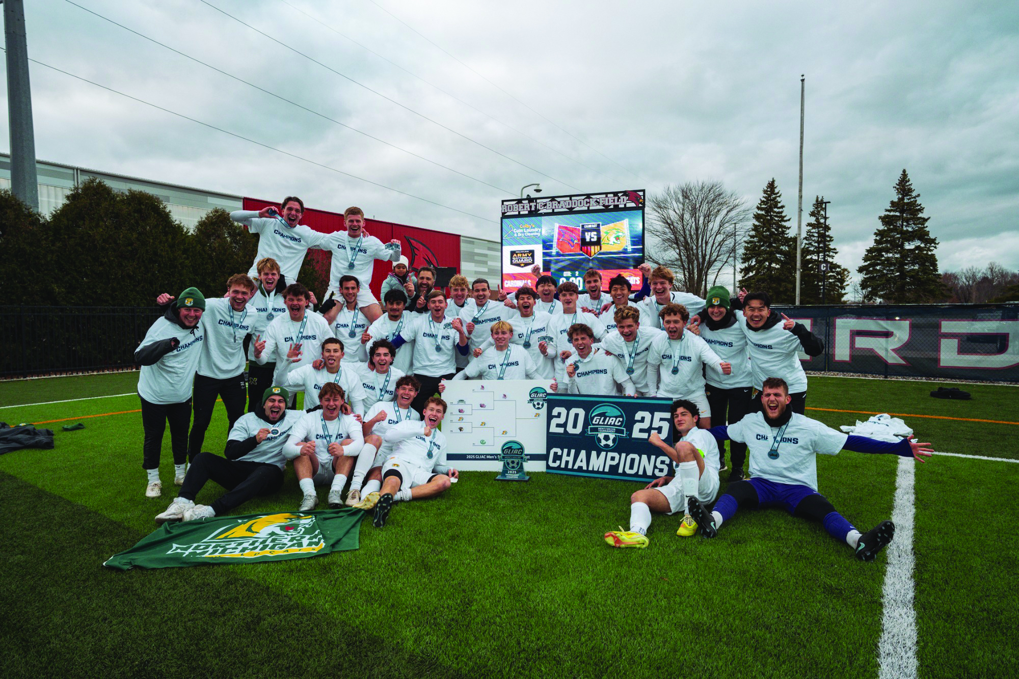NMU's Men's Soccer team holding the 2025 GLIAC Championship banner.