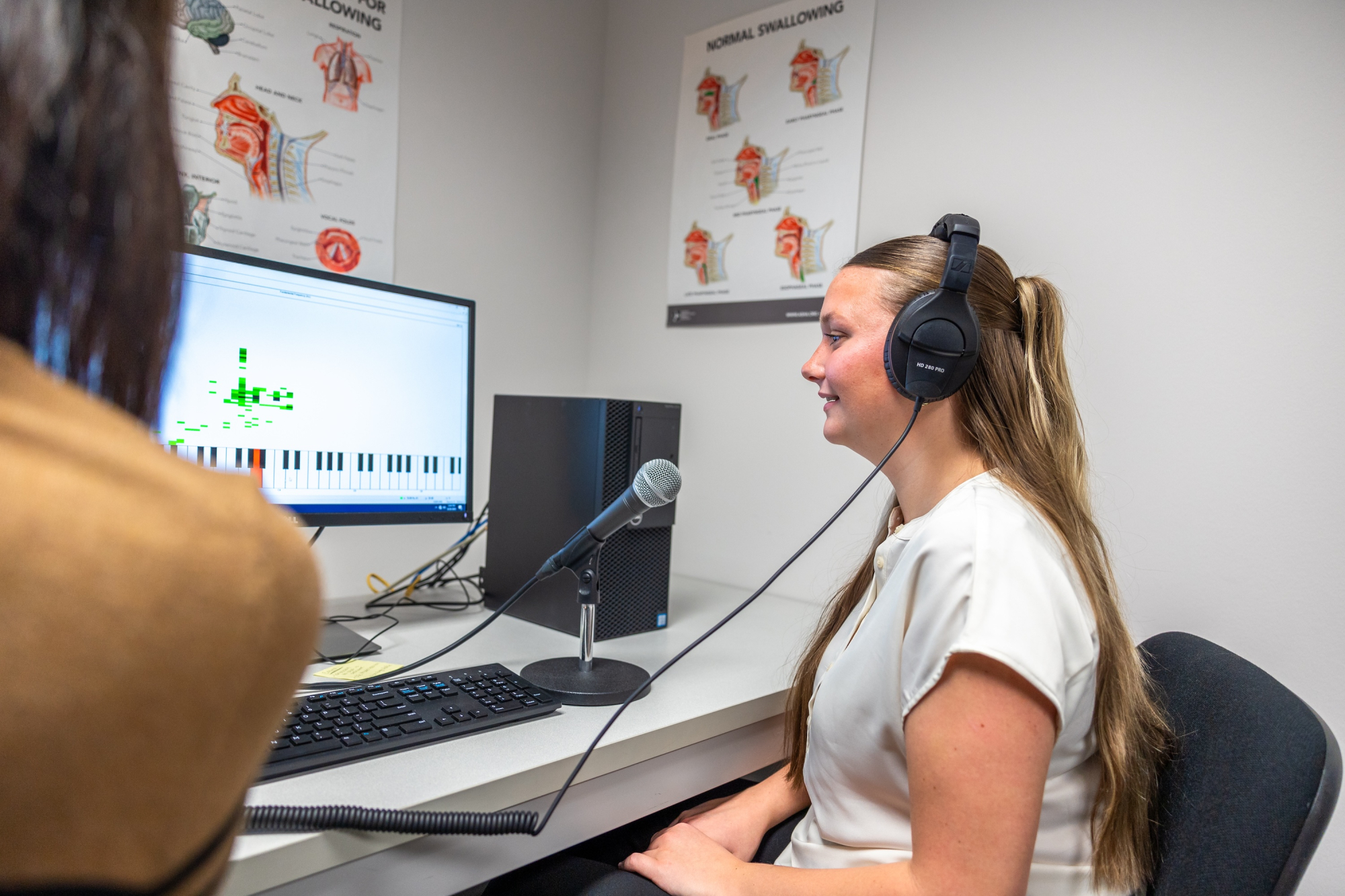Speech, Language, Hearing science student sits at computer with microphone while wearing headphones
