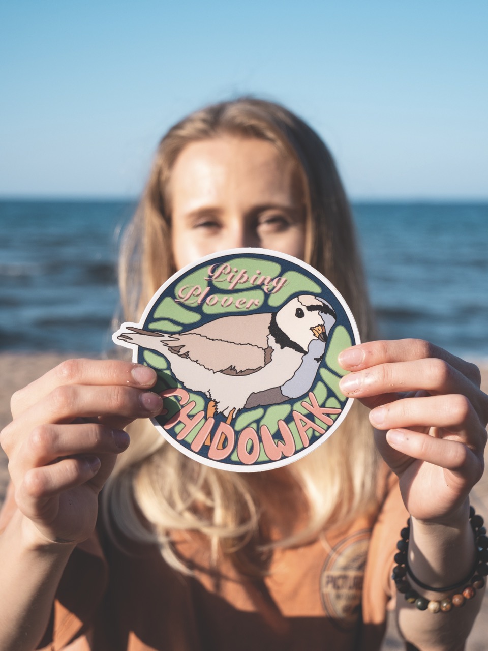 Marissa Burkman holding a sticker of a chidowak (piping plover)