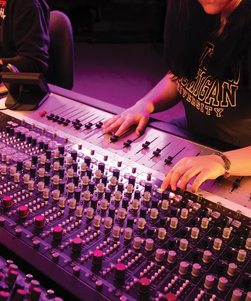 Student in Northern Michigan University t-shirt at large studio production control panel