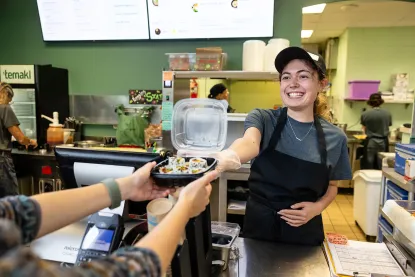 Student handing sushi order to guest