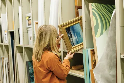 Emily Lanctot pulling small framed painting of waterscape from shelf