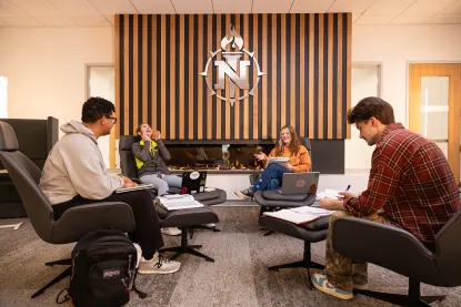 Four student sitting in chairs around a fireplace in the newly renovated Harden Hall.
