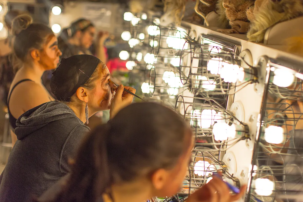 Students putting on makeup with mirrors and many lightbulbs