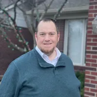 Man smiling at the camera in front of a house