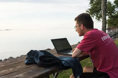 Student working on laptop by lake superior