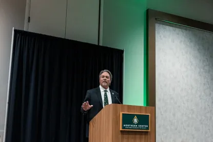 Dr. Olsen standing at a podium addressing the NMU community.