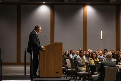 President Olsen speaking at a podium on stage to a room of people.