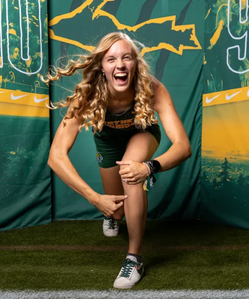 Athlete leaning into the camera in front of green backdrop containing gold outline of the U.P.