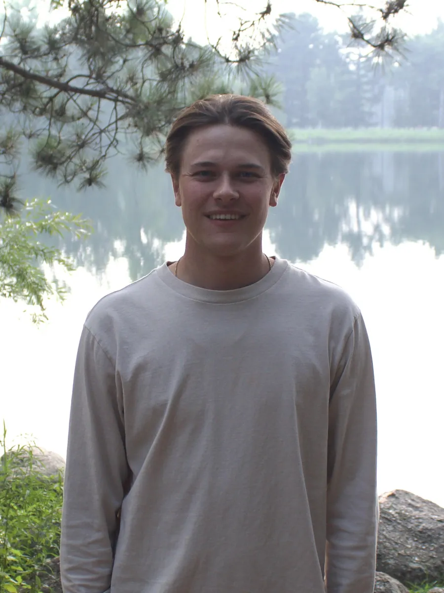 Graduate assistant Grant Atwood smiling by a pond