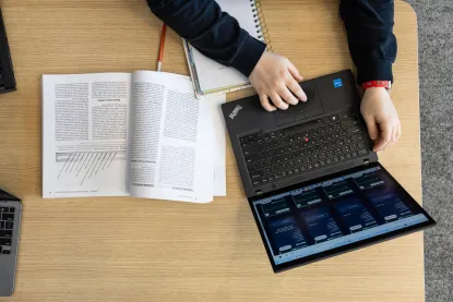Student working on a laptop with an open textbook and notebook beside them.