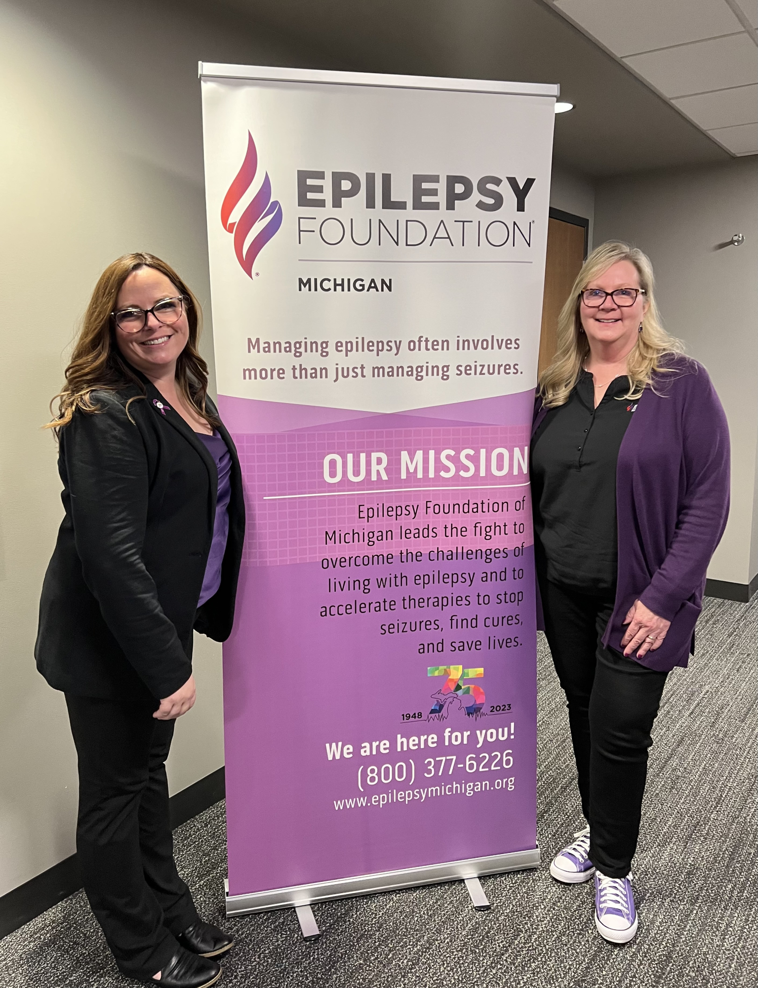 Two representatives of the Epilepsy Foundation of Michigan stand in front of a Foundation banner