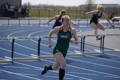 Sydney running on a track with hurdles behind her. 