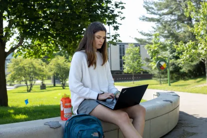 NMU student sitting outside using a laptop computer.