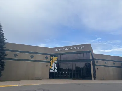 The exterior of Berry Events Center, a large building with tan walls, geometric designs, and dark tinted windows, under a partly cloudy blue sky. A graphic of a wildcat is visible on the glass entryway.