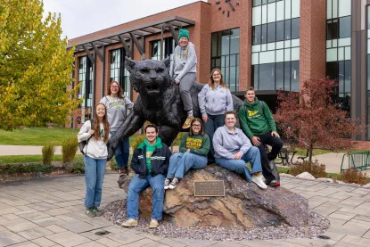 Eight NMU students gathered around the wildcat statue on NMU's campus.