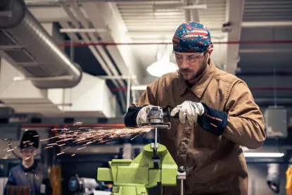 NMU welding student uses a grinder on a piece of metal in a welding lab.