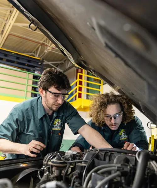 Two NMU automotive technology students work together under the hood of a vehicle in an automotive lab.