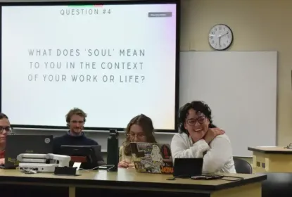Three students sitting on a panel discussion for a class project. The screen projects the the slide "What does 'soul' mean to you in the context of your work or life?"