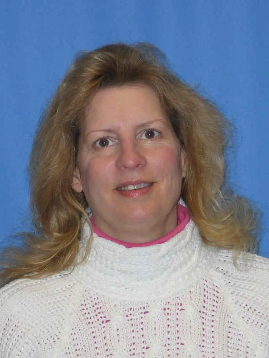 Photo of a woman with blonde hair and a white sweater with a blue background.