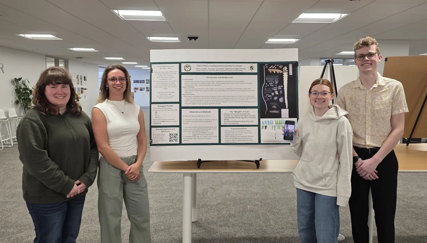 Four students standing next to a poster