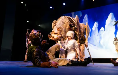 A polar bear puppet looms over a student onstage during a performance of ABOVE THE TIMBERLINE