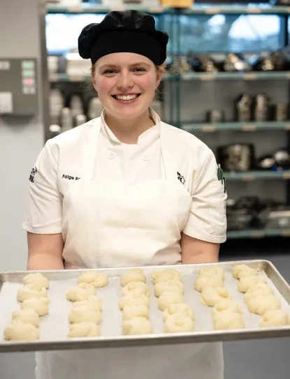 Female student smiling as she holds a tray of dough ready to go in the oven.