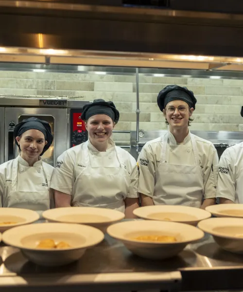 Hospitality students smile for the camera behind the open kitchen line