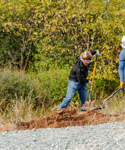 Two students in hard hats dig with shovels