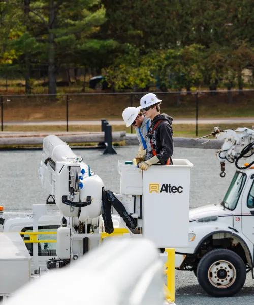 Two students in hard hats in a bucket truck.