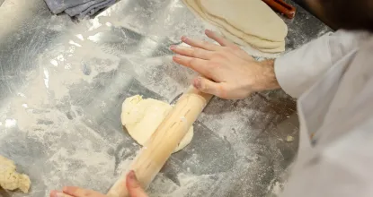Student rolls out dough pm a floured countertop using a wooden rolling pin.