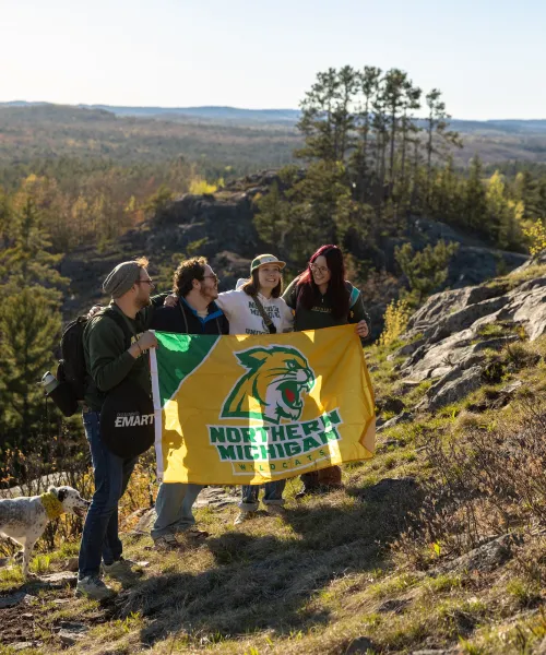 Students holding NMU flag on top of a mountain 