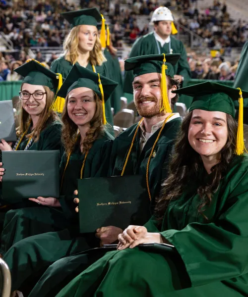 Students show off their diplomas while sitting in the audience in their NMU graduation regalia