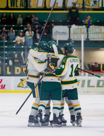 NMU Hockey players in a huddle celebrating on the ice