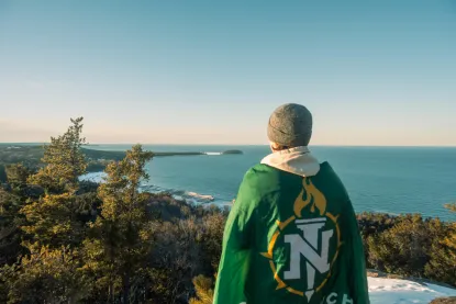 Student wrapped in an NMU flag while overlooking Lake Superior.