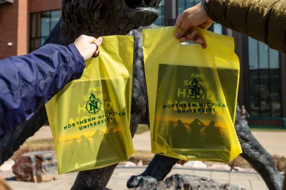 Two people holding campus visit bags in front of NMU's wildcat statue.