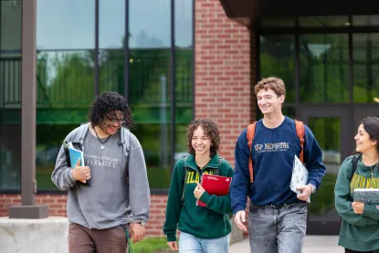 Three students walking with backpacks and books on NMU's campus