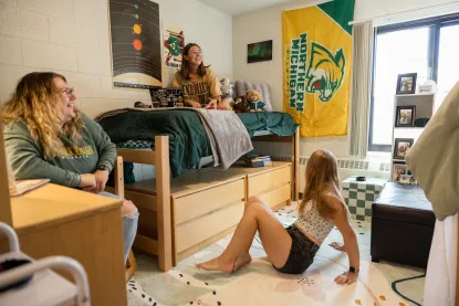 Three female students handing out in an NMU dorm room with a Northern Michigan University Wildcat flag on the wall
