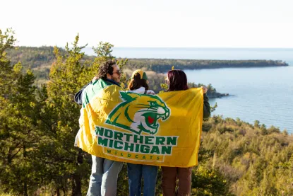 Three students hold a Northern Michigan University wildcat flag behind their back