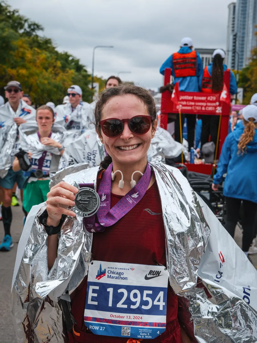 Woman in running attire, wrapped in a post-race blanket and holding a medal.