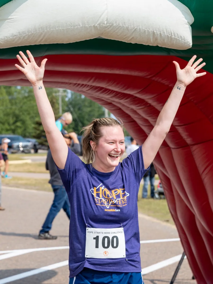 Woman cheering with arms overhead at finish line.