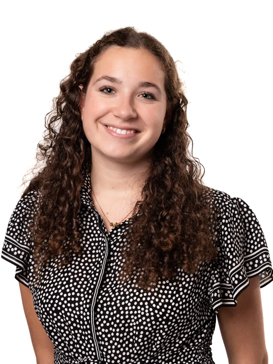 Headshot of student. She has curly dark hair and is wearing a black shirt with white pattern.