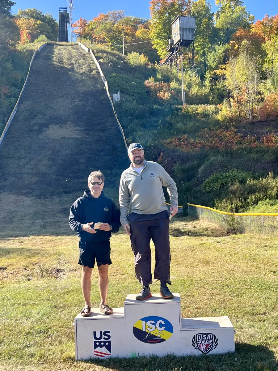 Image of two men on three tiered podium with a scenic hill behind.