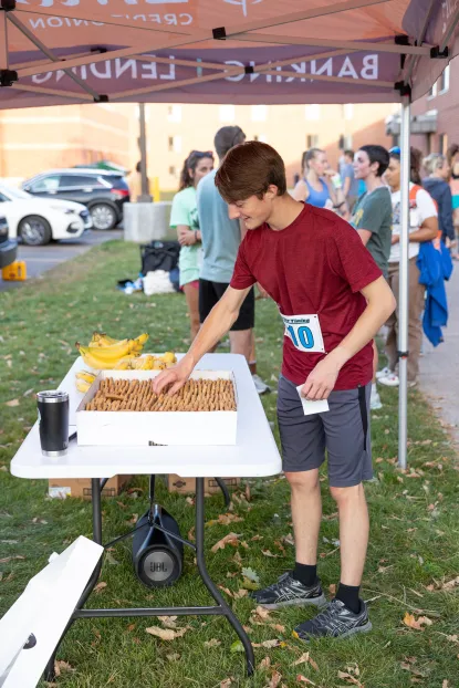 A student wearing a red shirt and gray shorts grabs a cookie from the post-race refreshment tent.